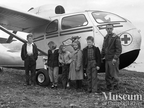 Group of children with pilot beside BC Airlines airplane